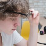 Nastolatek zdejmujący okulary i mrużący oczy – możliwe objawy zmęczenia wzroku lub wady refrakcji podczas nauki przy biurku.