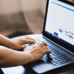 Osoba korzystająca z laptopa, siedząca przy stole i wpisująca coś na klawiaturze. Na ekranie widać otwartą przeglądarkę internetową