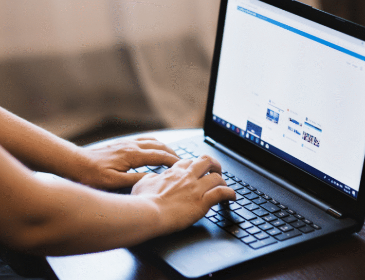 Osoba korzystająca z laptopa, siedząca przy stole i wpisująca coś na klawiaturze. Na ekranie widać otwartą przeglądarkę internetową