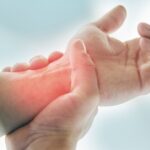 Osoba trzymająca się za nadgarstek, wskazująca na ból lub stan zapalny – możliwe objawy osteoporozy lub chorób stawów.