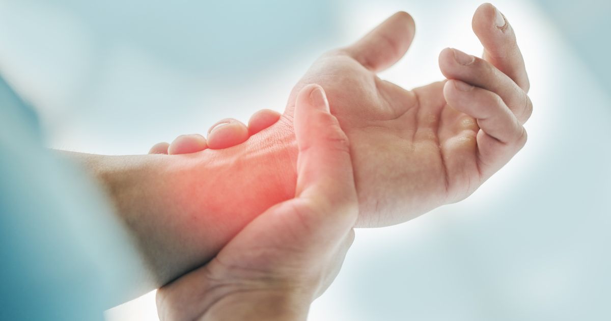 Osoba trzymająca się za nadgarstek, wskazująca na ból lub stan zapalny – możliwe objawy osteoporozy lub chorób stawów.