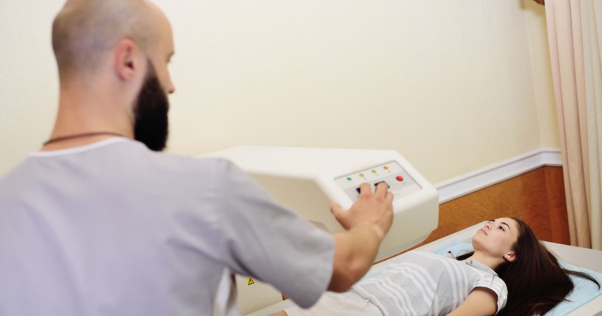 Badanie densytometryczne u młodej kobiety – technik obsługuje aparat do pomiaru gęstości kości.