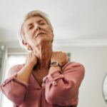 Starsza kobieta z bólem karku trzymająca się za szyję – objawy zwyrodnień kręgosłupa szyjnego