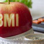 Czerwona jabłko z napisem BMI, otoczone miarką krawiecką i kalkulatorem – symbol obliczania wskaźnika masy ciała i kontroli wagi.