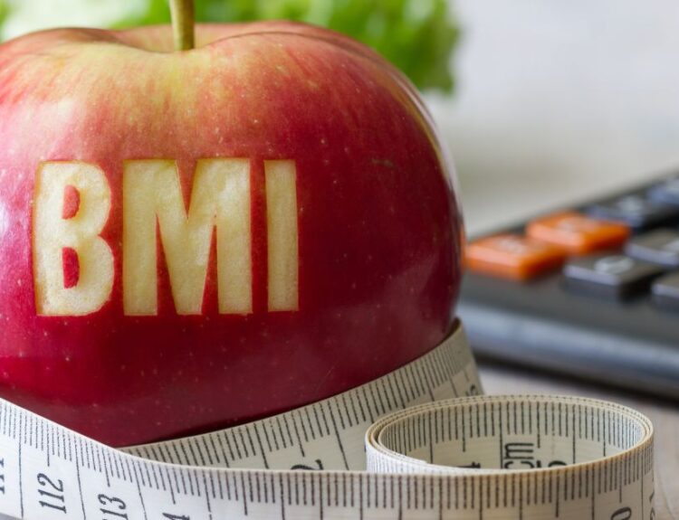 Czerwona jabłko z napisem BMI, otoczone miarką krawiecką i kalkulatorem – symbol obliczania wskaźnika masy ciała i kontroli wagi.
