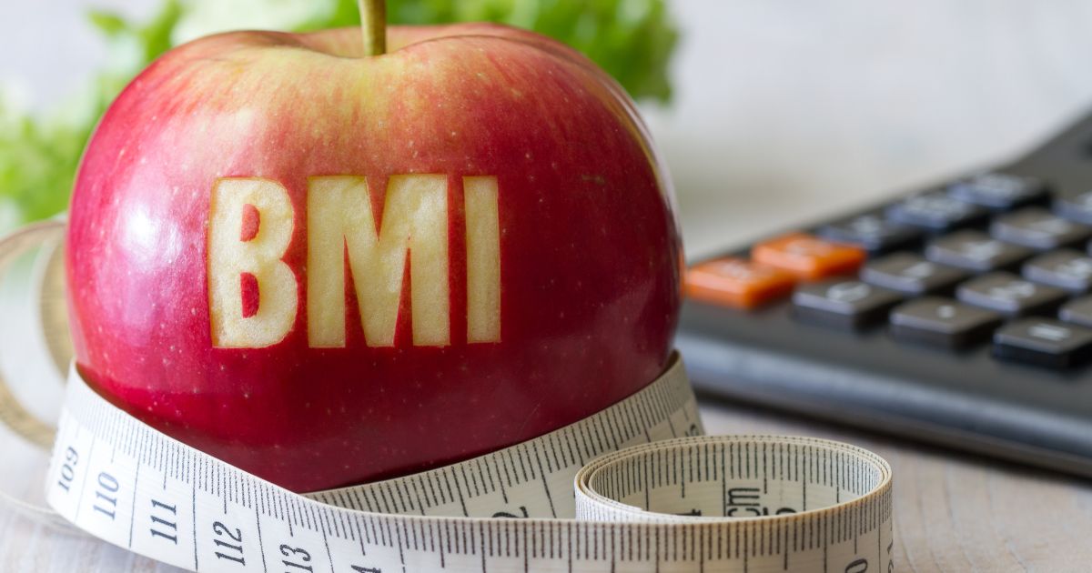 Czerwona jabłko z napisem BMI, otoczone miarką krawiecką i kalkulatorem – symbol obliczania wskaźnika masy ciała i kontroli wagi.