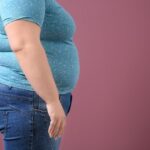 Osoba z nadwagą w pozycji bocznej na tle różowej ściany, widoczny brzuch i biodra