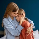Zatroskana matka przytula smutną córkę, próbując ją pocieszyć – scena ukazująca wsparcie emocjonalne i bliską więź w trudnej chwili