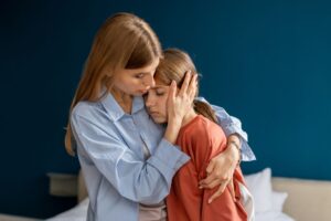 Zatroskana matka przytula smutną córkę, próbując ją pocieszyć – scena ukazująca wsparcie emocjonalne i bliską więź w trudnej chwili