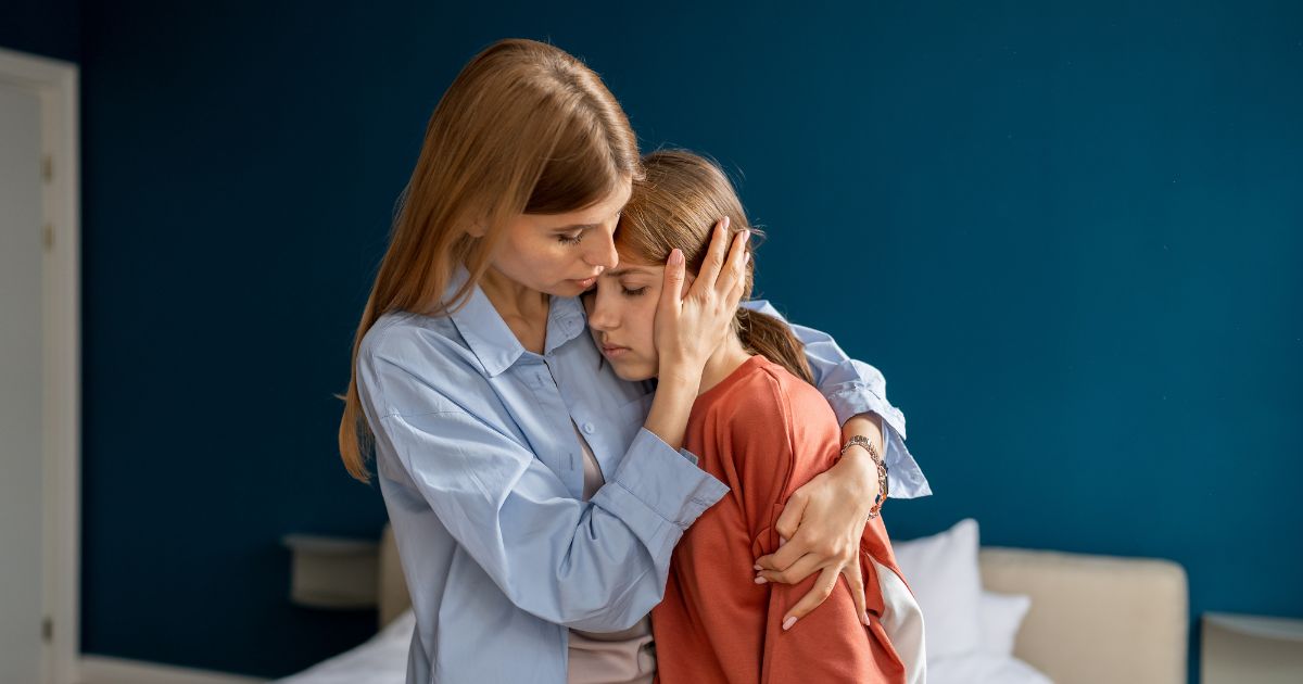 Zatroskana matka przytula smutną córkę, próbując ją pocieszyć – scena ukazująca wsparcie emocjonalne i bliską więź w trudnej chwili